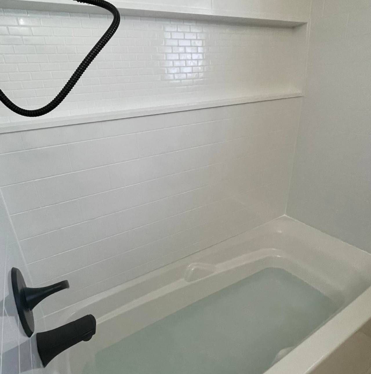 A bathtub in a bathroom with white tiles and black faucets.
