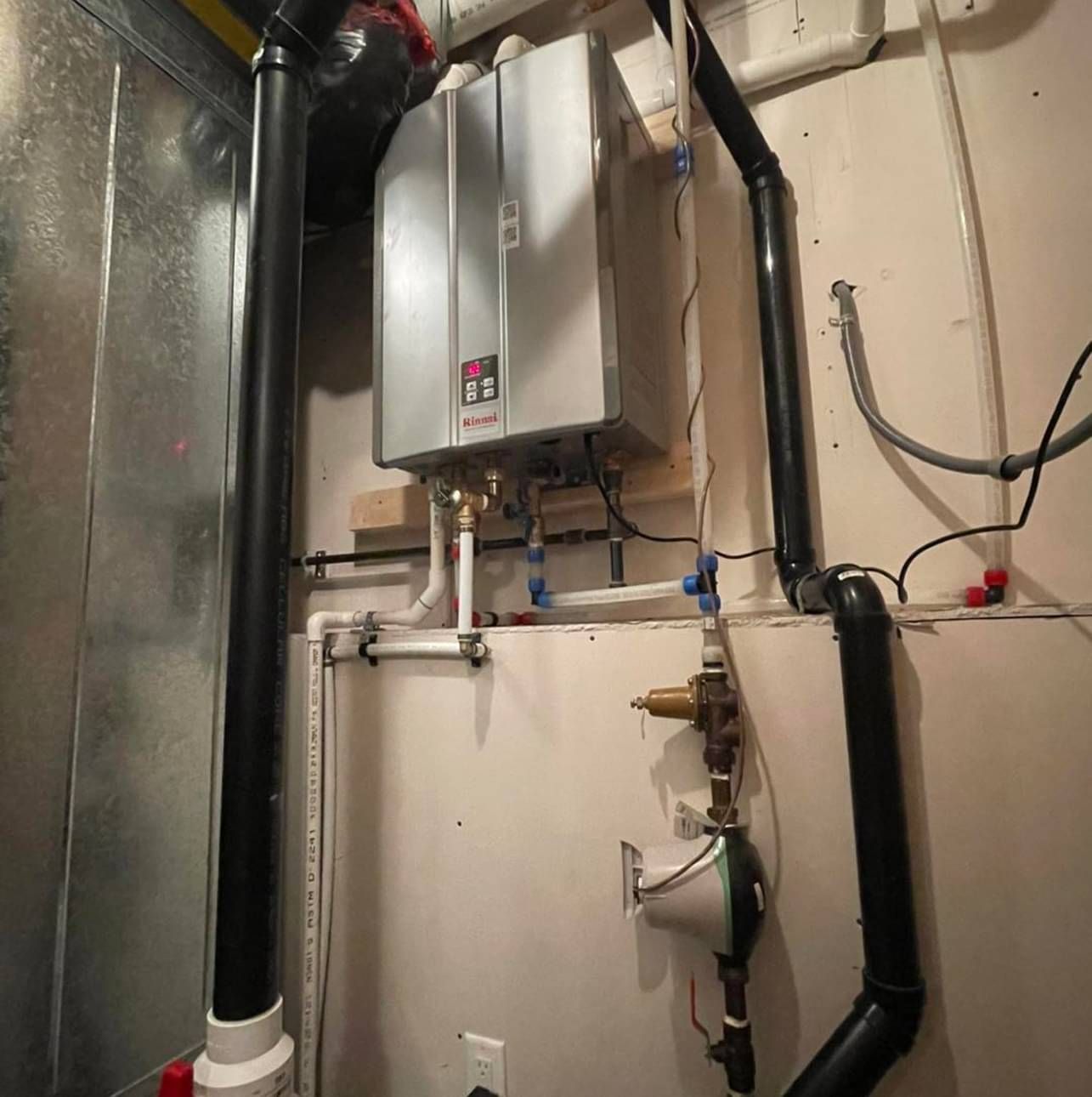 A water heater is hanging on a wall next to a bunch of pipes.