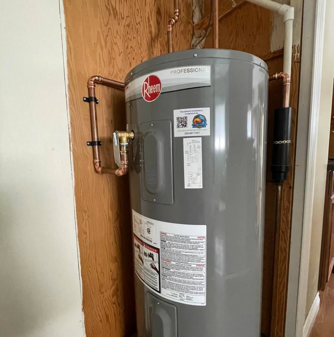 A gray water heater is sitting next to a wooden wall.