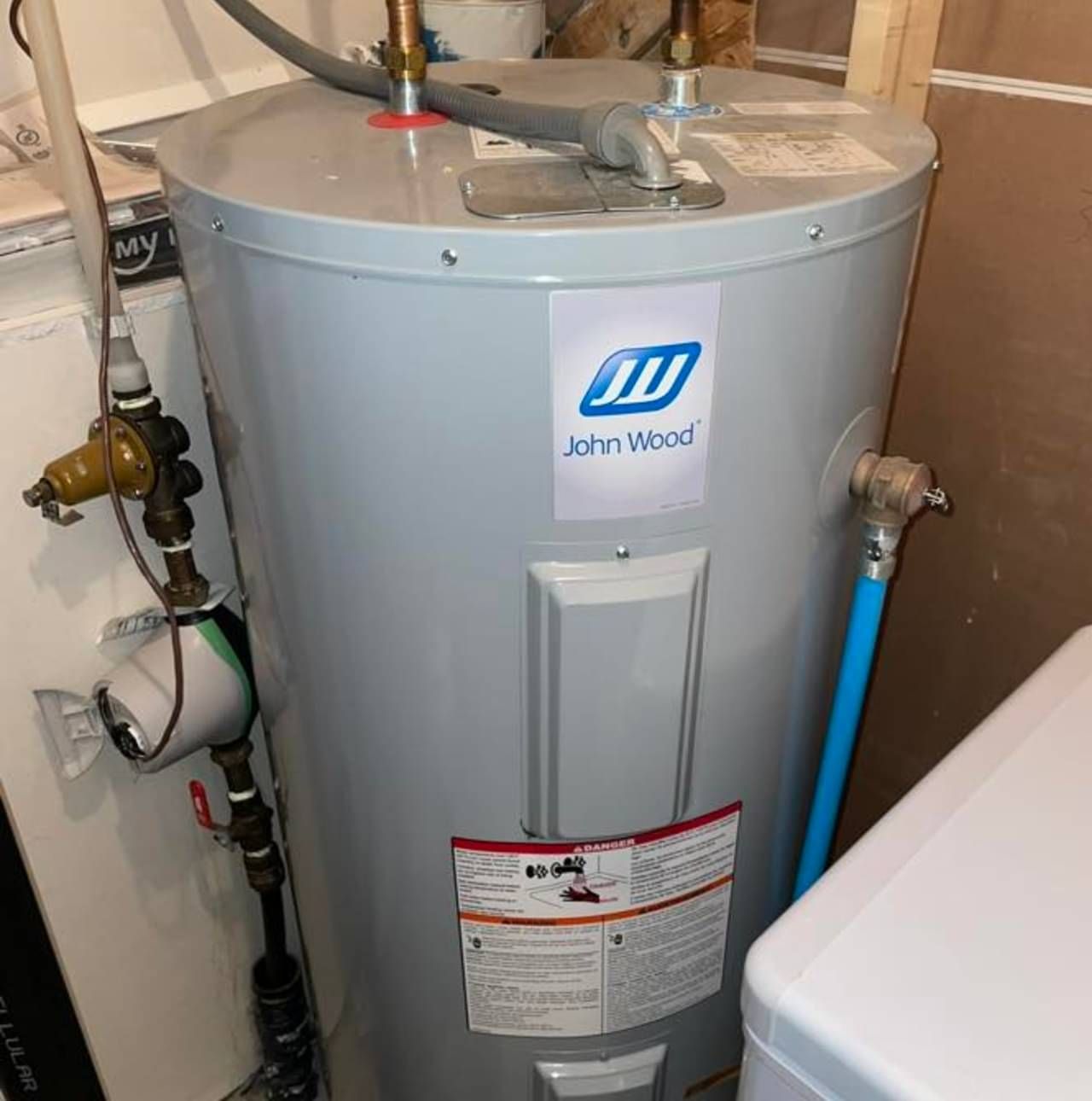 A john wood water heater is sitting next to a washer and dryer.