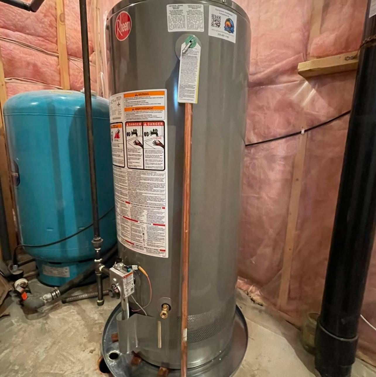 A water heater is sitting in a room next to a blue tank.