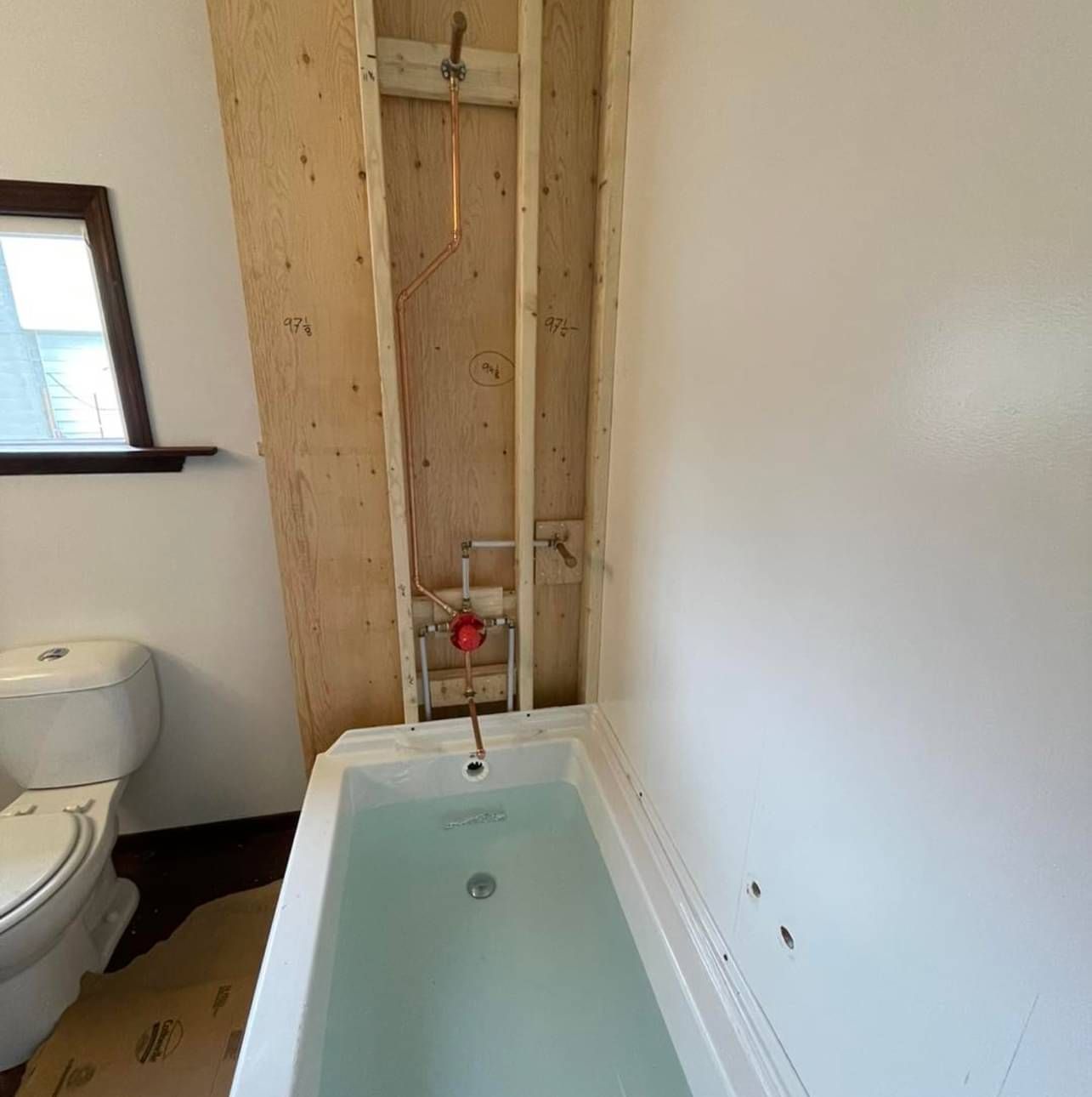 A bathroom with a bathtub , toilet and mirror.