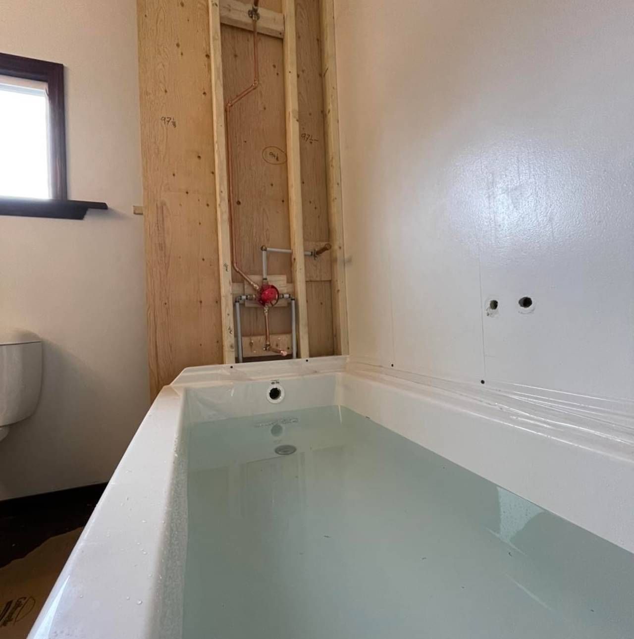 A bathtub filled with water in a bathroom next to a toilet.