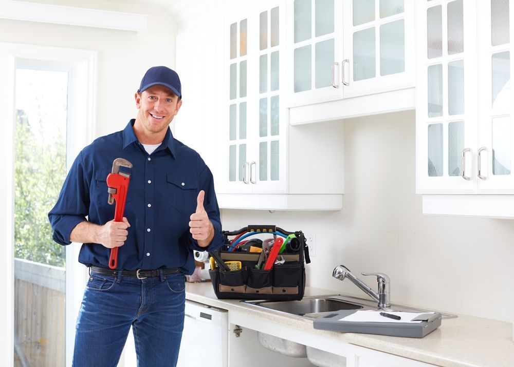 Plumber holding wrench, giving thumbs-up in a kitchen with tools.