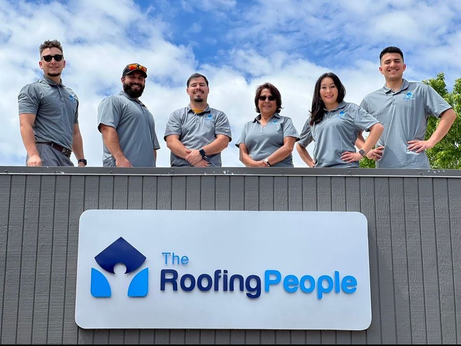 A group of people standing in front of a sign that says the roofing people.
