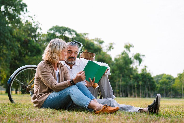 couple sitting on grass while reading a book