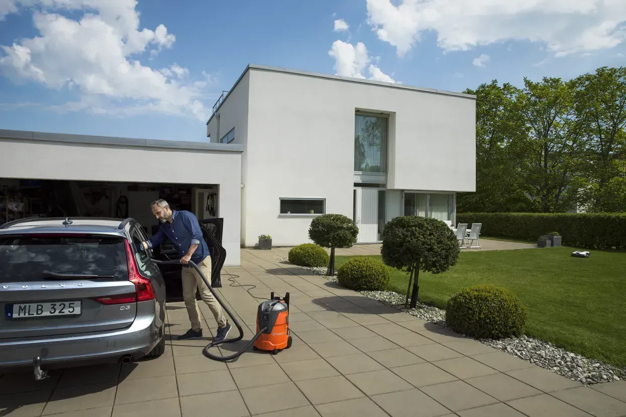 Mann mit Staubsuger der auf der Auffahrt eines Grundstückes sein Fahrzeug reinigt