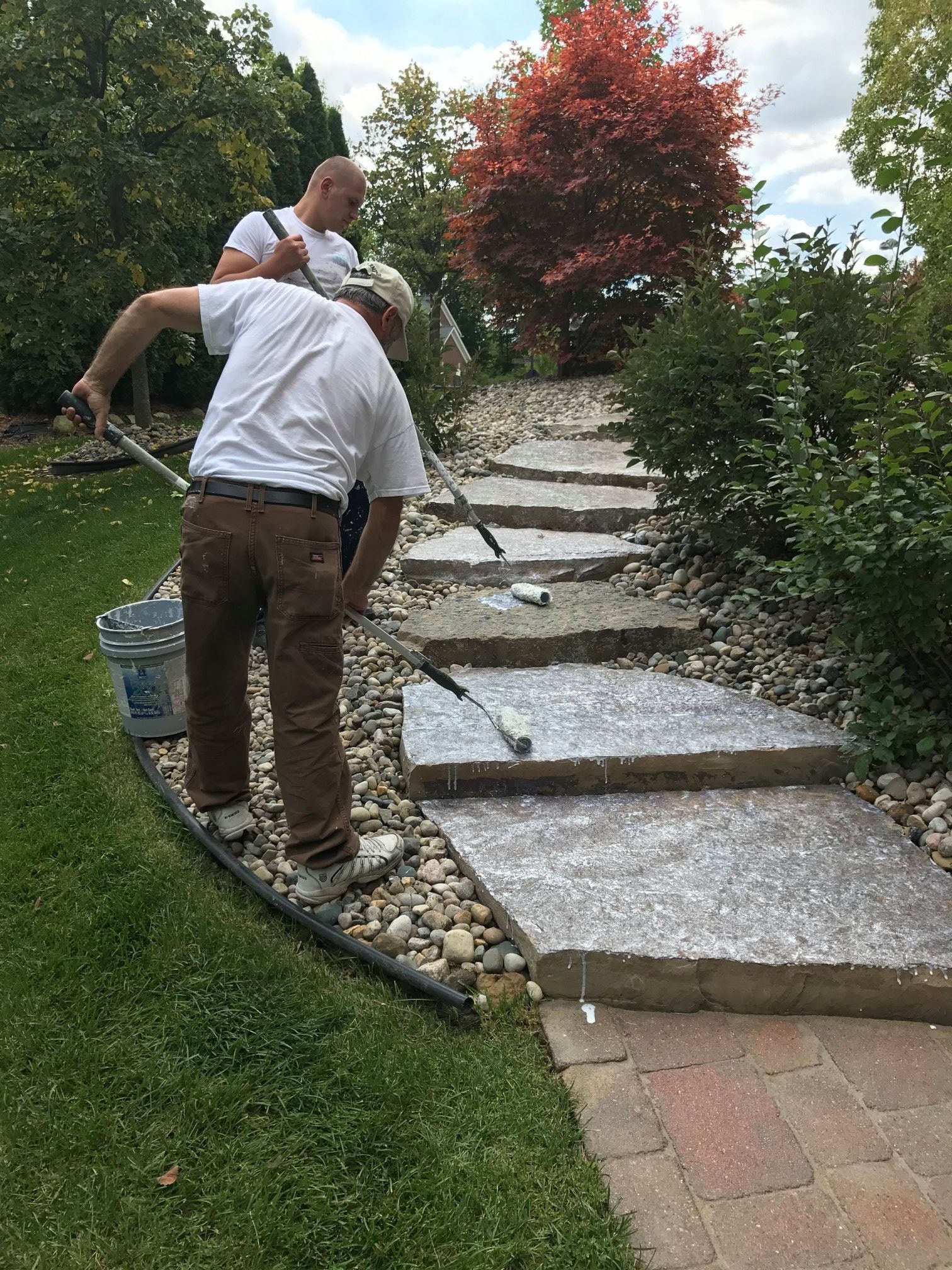 Two men are painting a stone walkway in a garden.