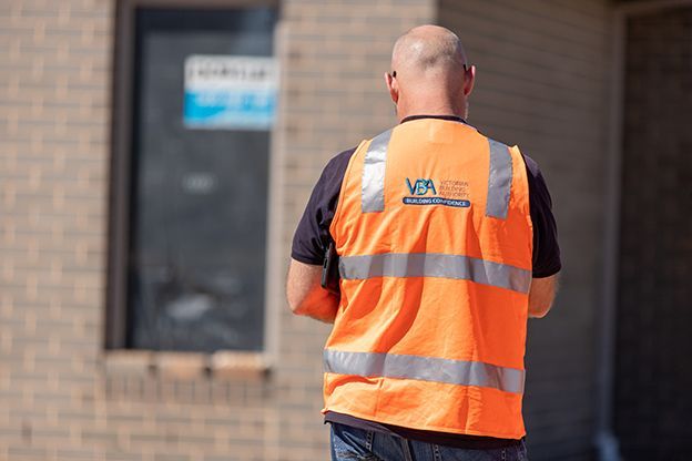 A man wearing an orange vest is standing in front of a building.