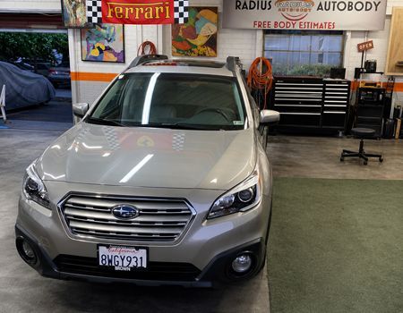 Silver Subaru parked in an auto body shop under Ferrari and Radius Auto Body signs.