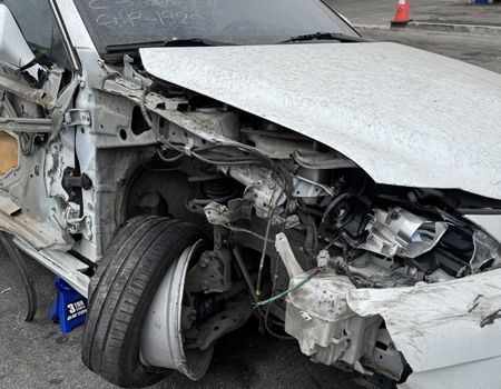 Severely damaged white car after a crash, with crushed front end and exposed wheel on a road