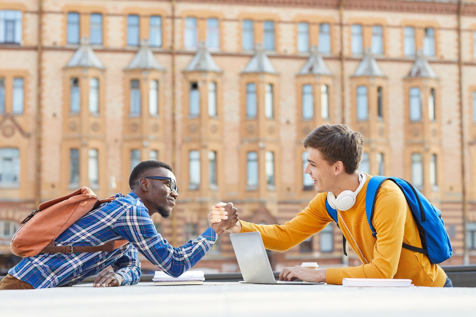 2 students shaking hands at a table with a laptop