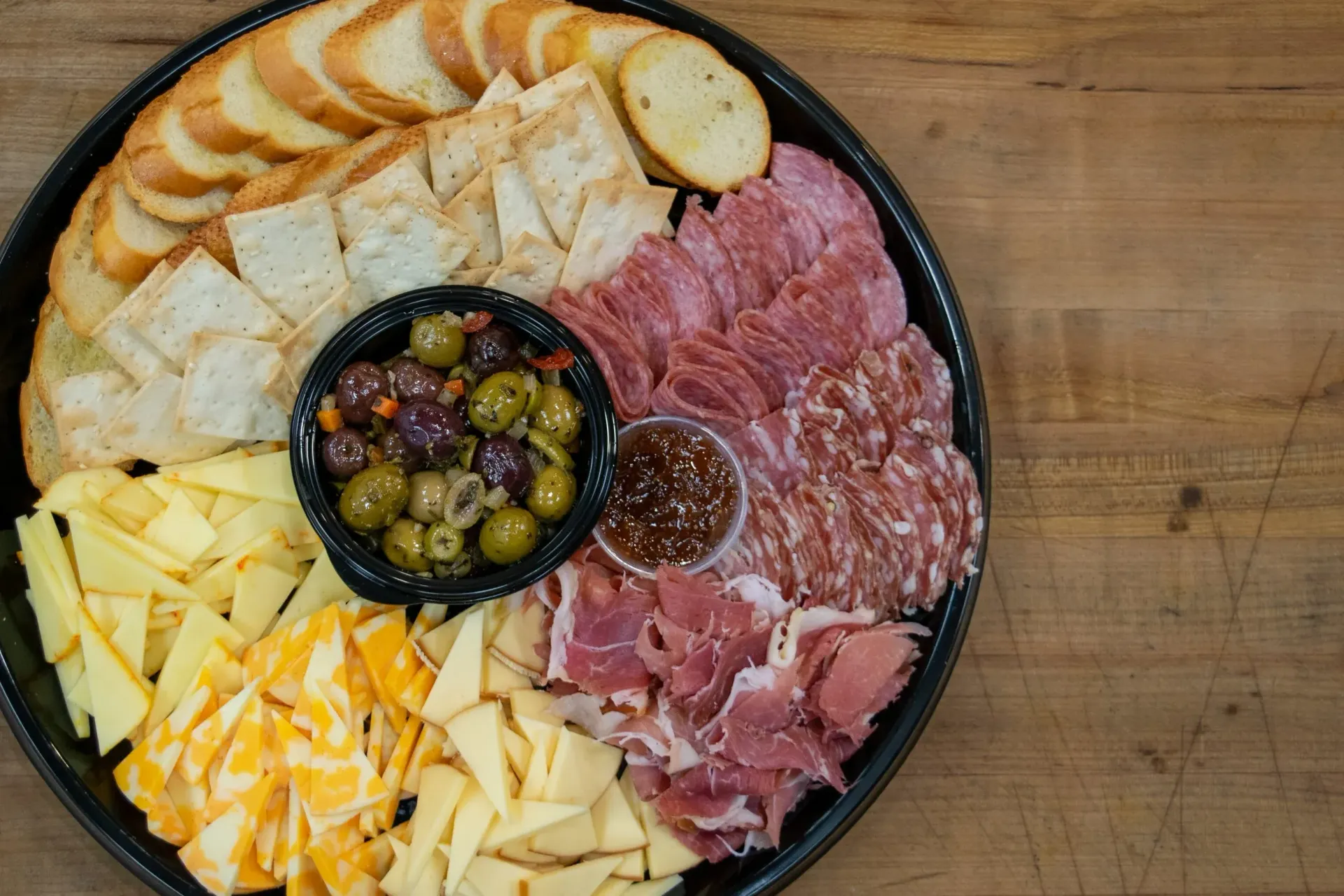 Charcuterie platter: bread, crackers, olives, meats, cheeses, and dipping sauces on a black tray.