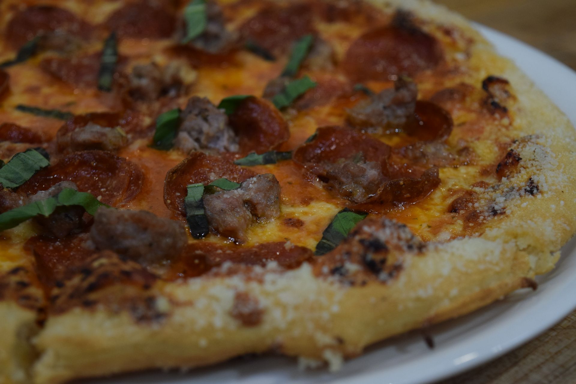 Pizza with pepperoni, sausage, basil on a white plate. Crust is golden brown.