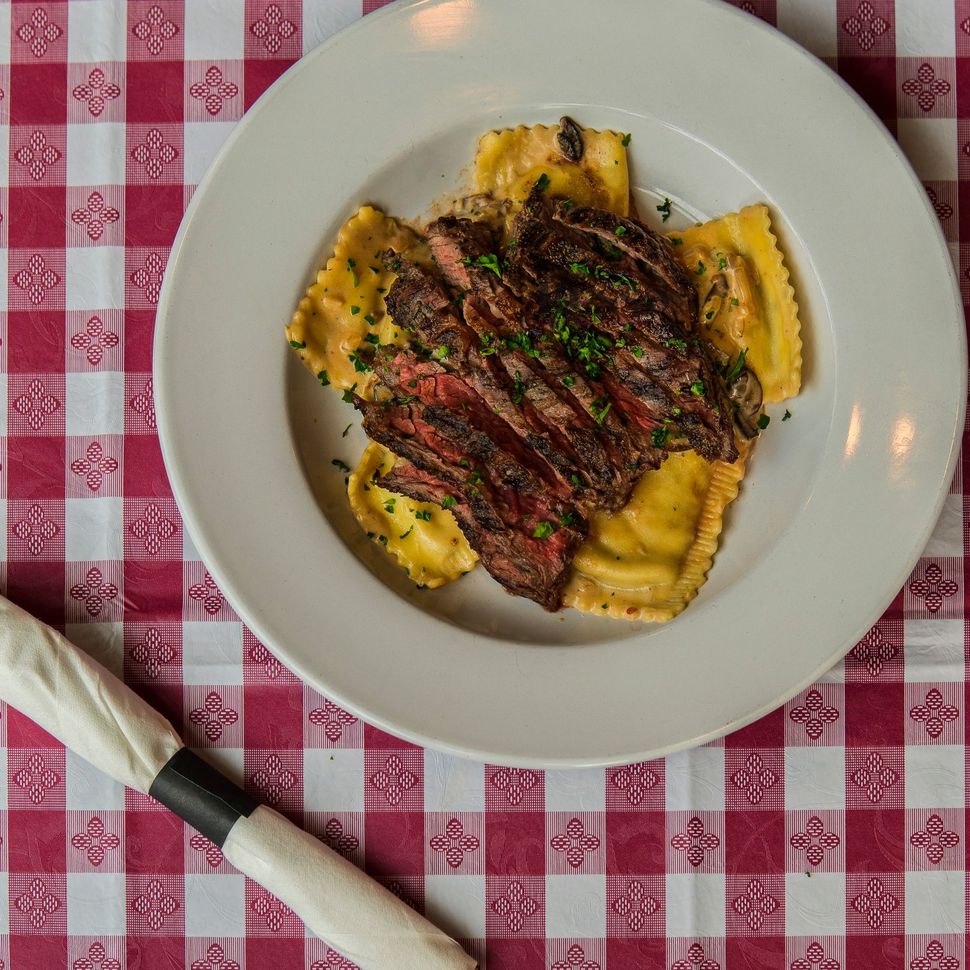 Steak and ravioli dish on a white plate, red checkered tablecloth.