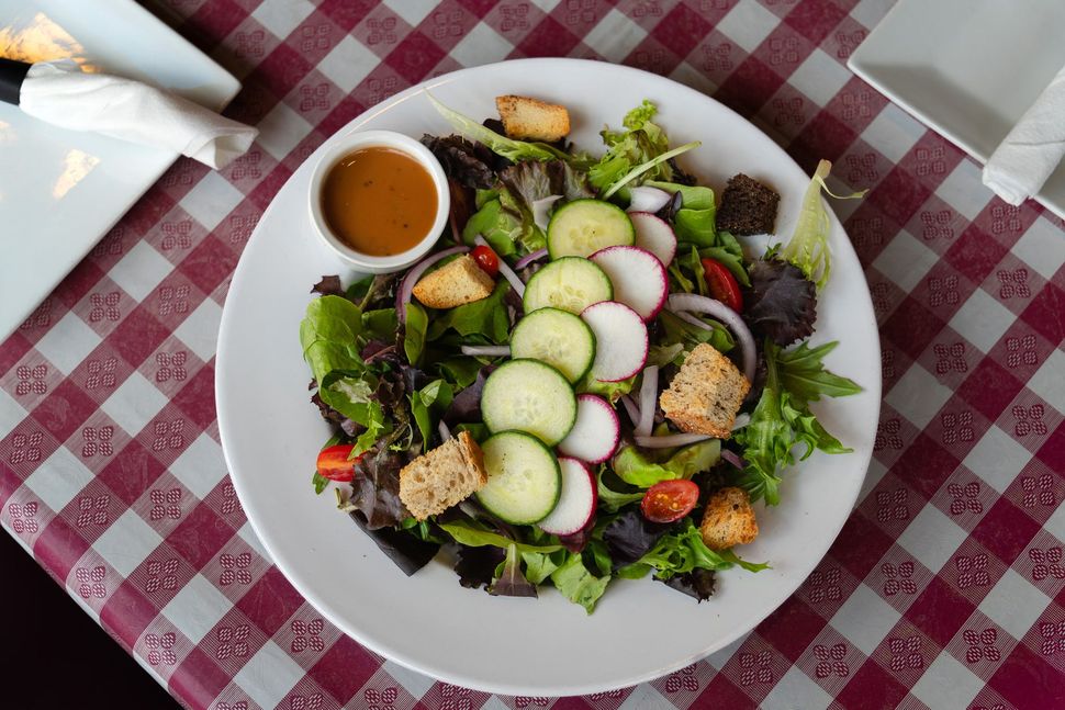 Salad on white plate with dressing. Includes cucumbers, radishes, and croutons on a checkered tablecloth.