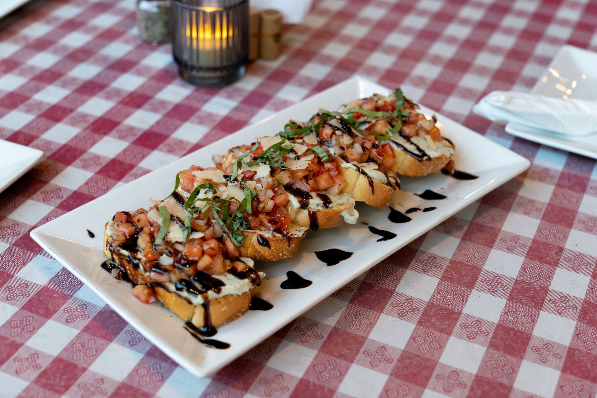 5 pieces of bread topped with tomatoes, basil, balsamic glaze and ricotta spread to make a bruschetta.