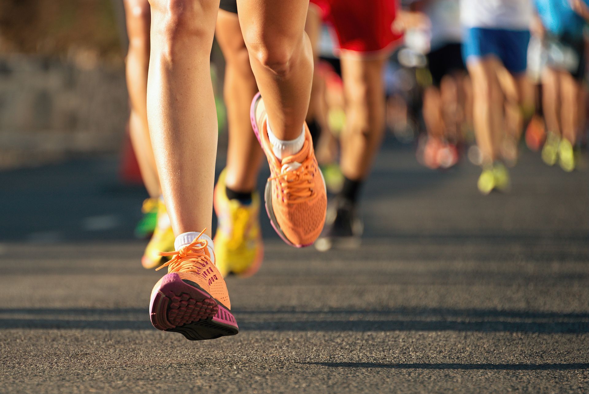 Runners' legs and shoes in motion on a paved road during a marathon, focus on orange sneakers.