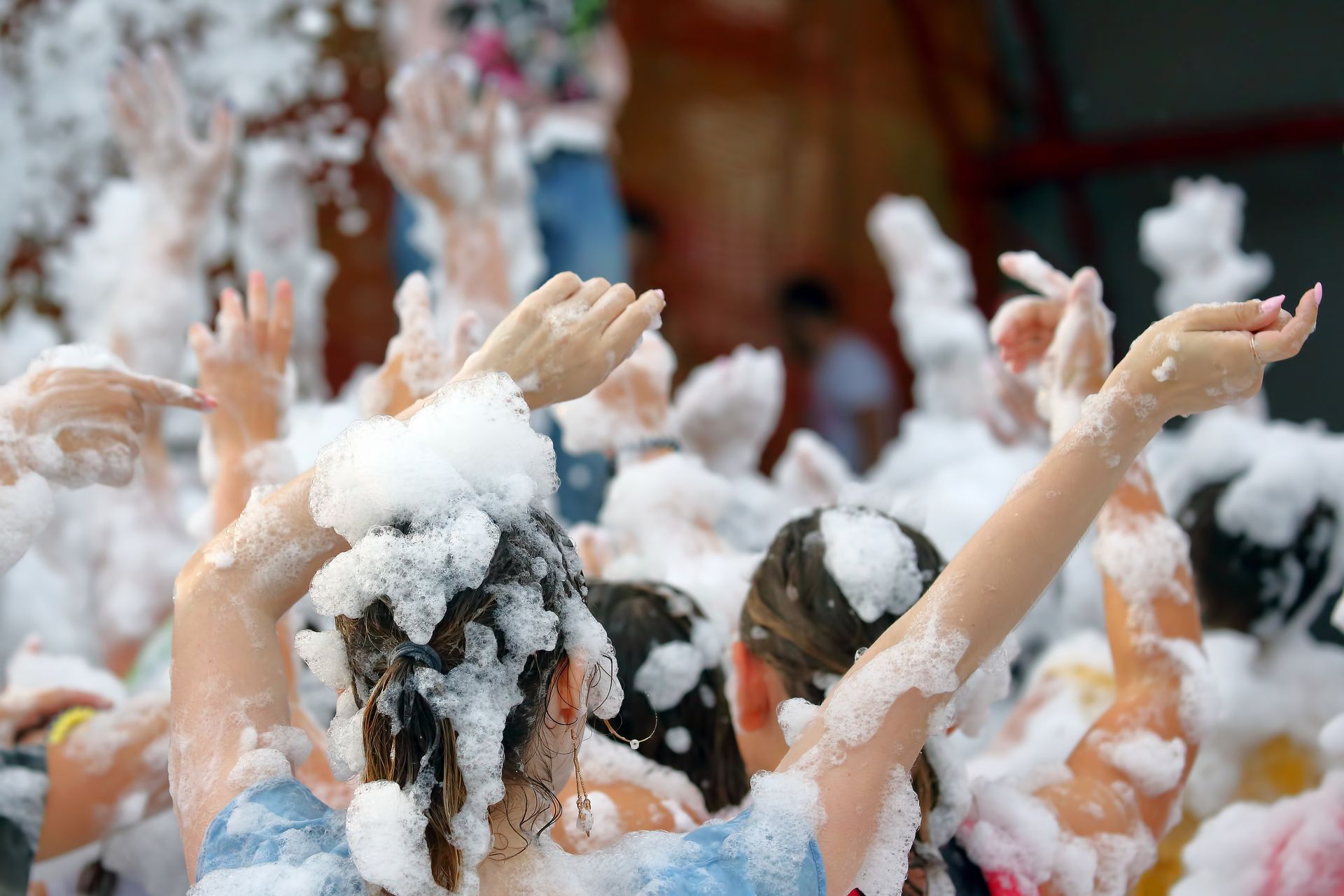 People with arms raised in the air, covered in white foam at a party.