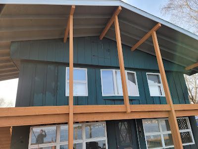 A green house with a lot of windows and a wooden deck.