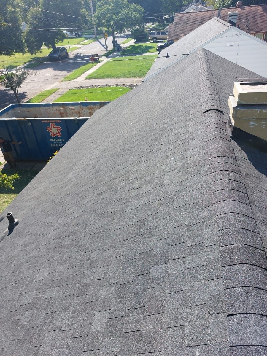 A black roof with a blue dumpster in the background