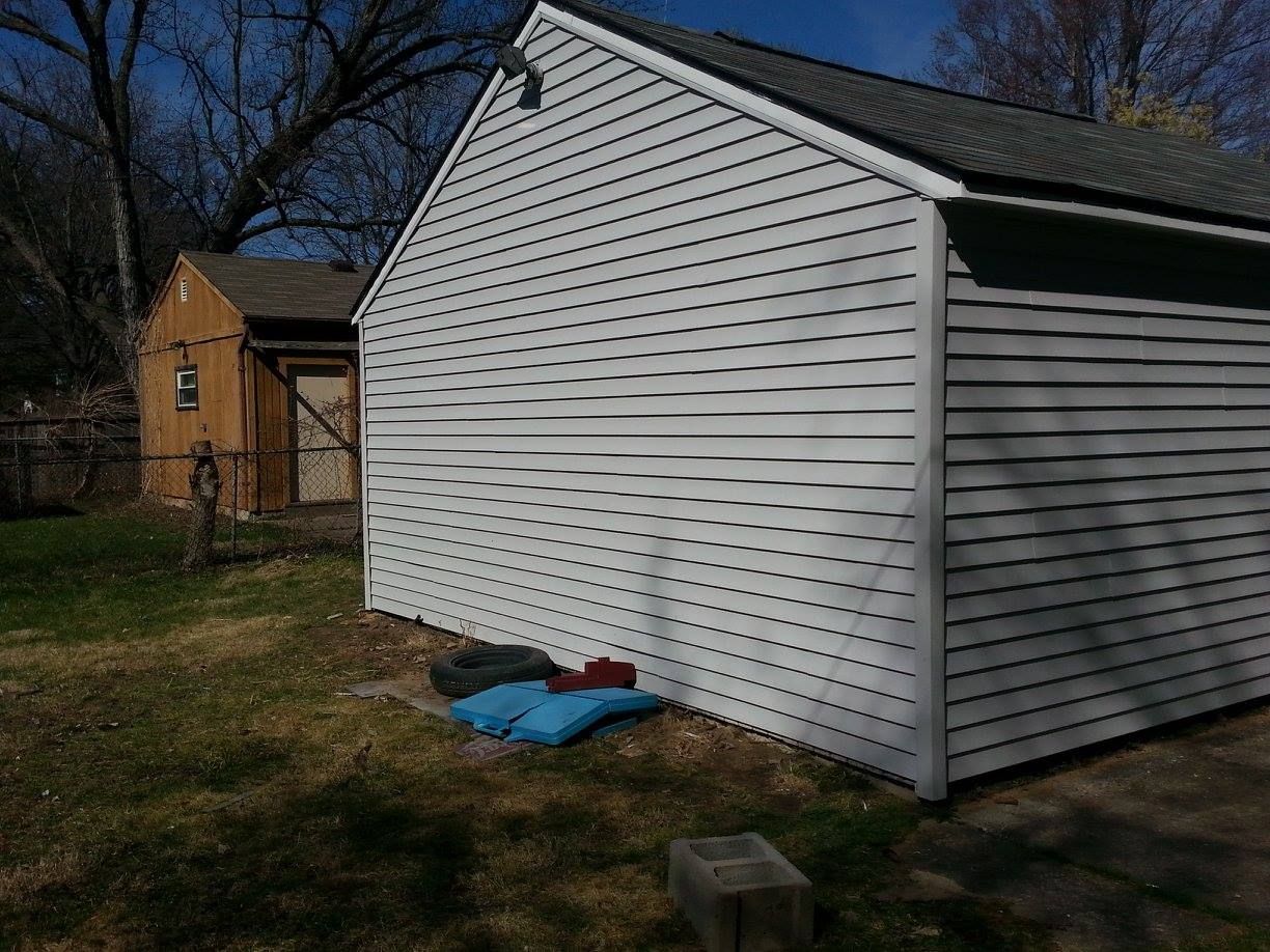 A white shed with holes in it is in the backyard of a house.