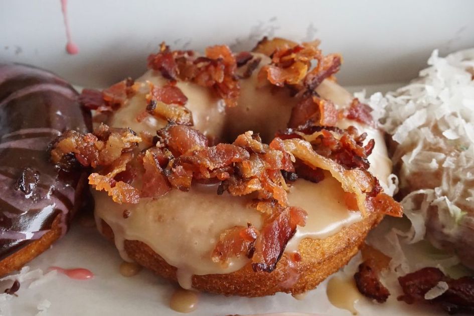 A close up of a bacon covered donut on a plate