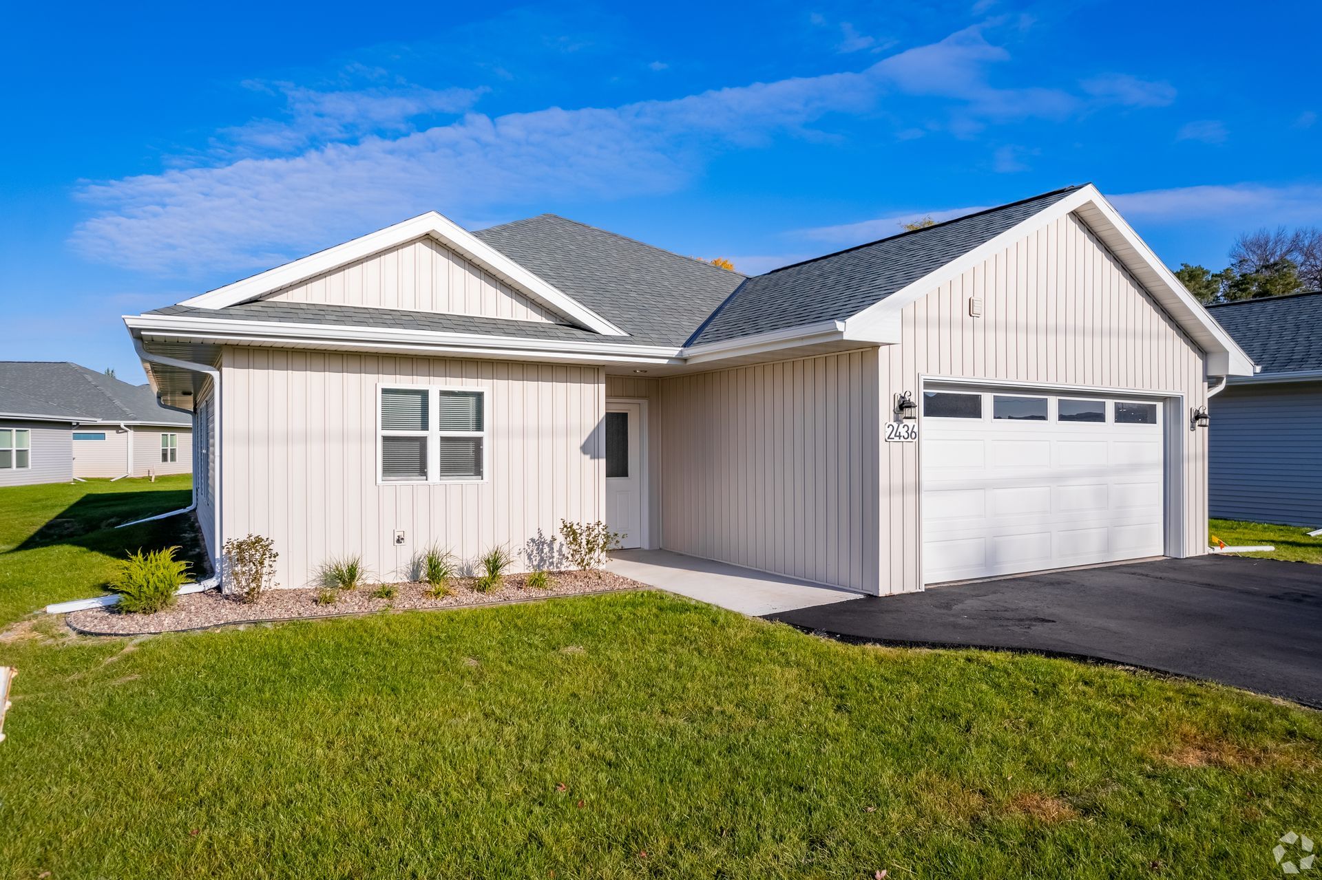 Single-story beige house with white trim, attached garage, and a green lawn on a sunny day