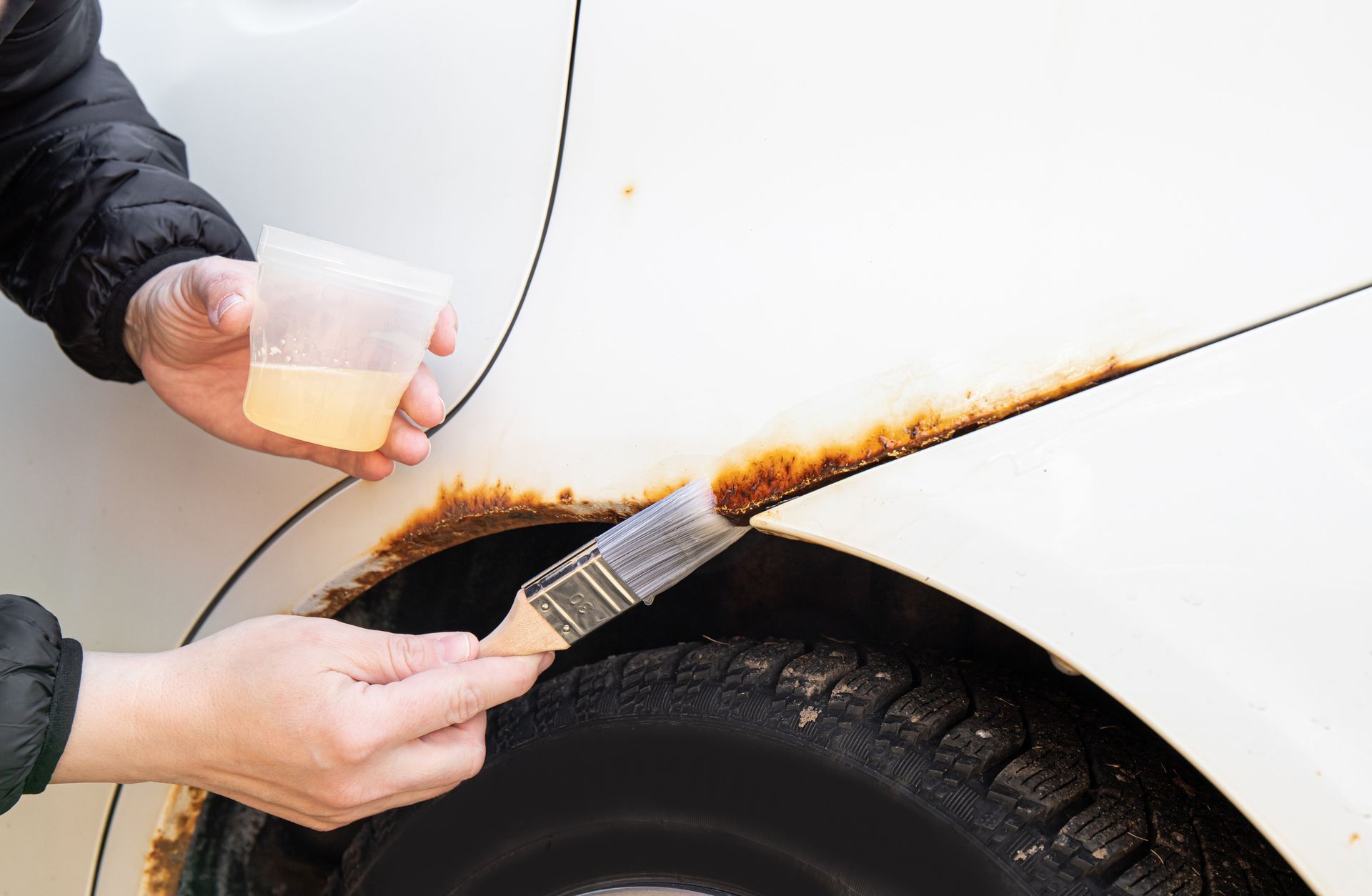 A person is using a brush to remove rust from a car fender | Pro Auto Repairs