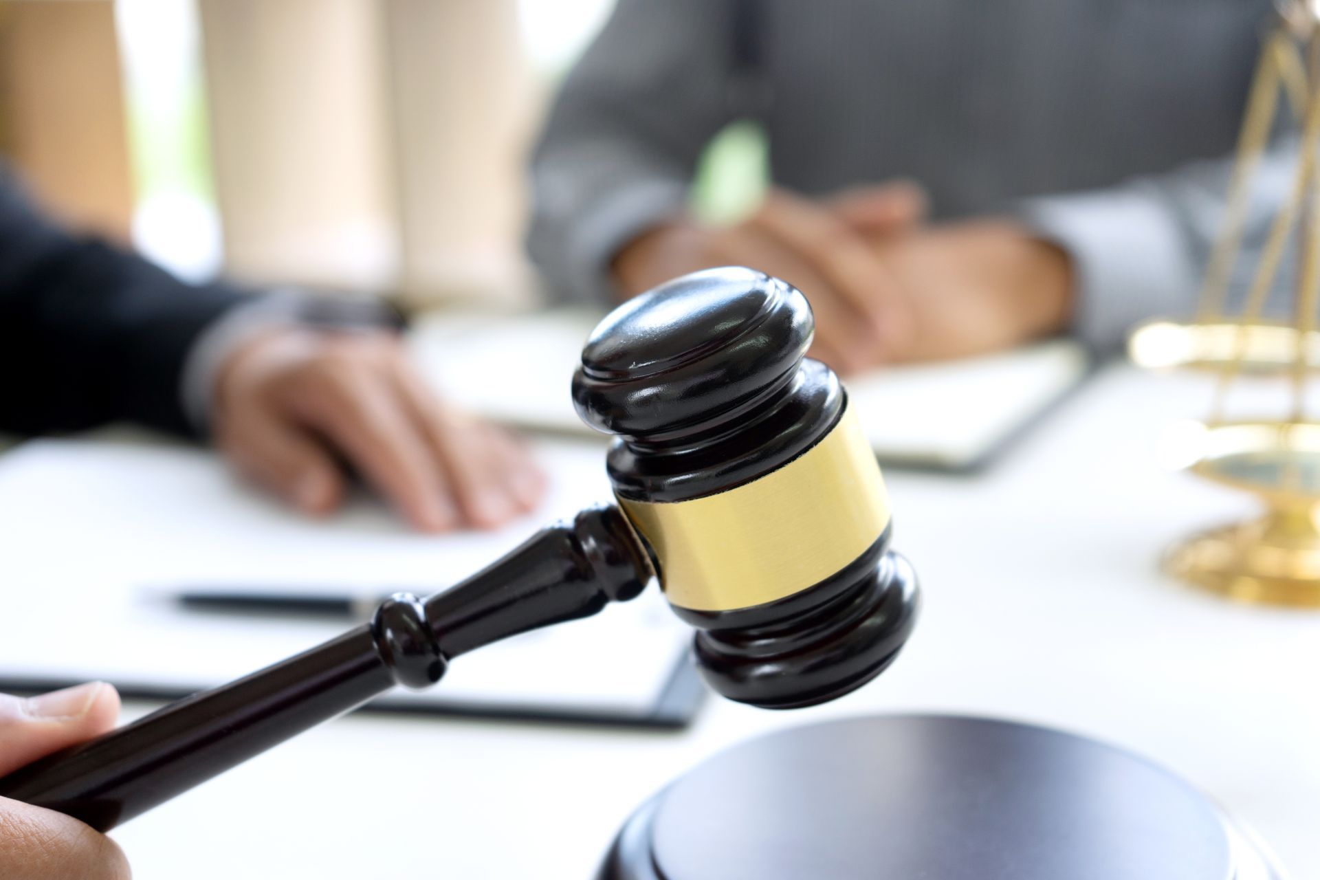 Gavel in hand, with blurred figures and scales of justice in background.