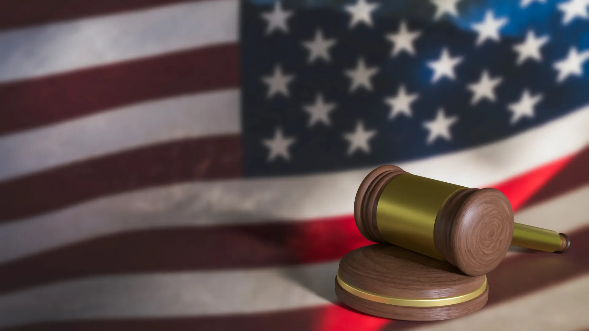 Gavel on sounding block, in front of blurred American flag. Legal system symbol.