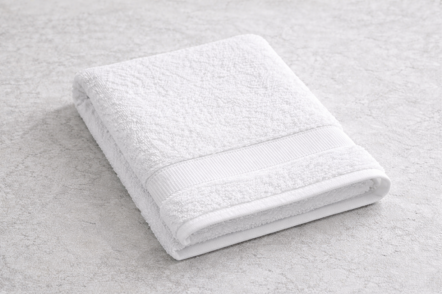 Folded white bath towel on a light-colored surface.