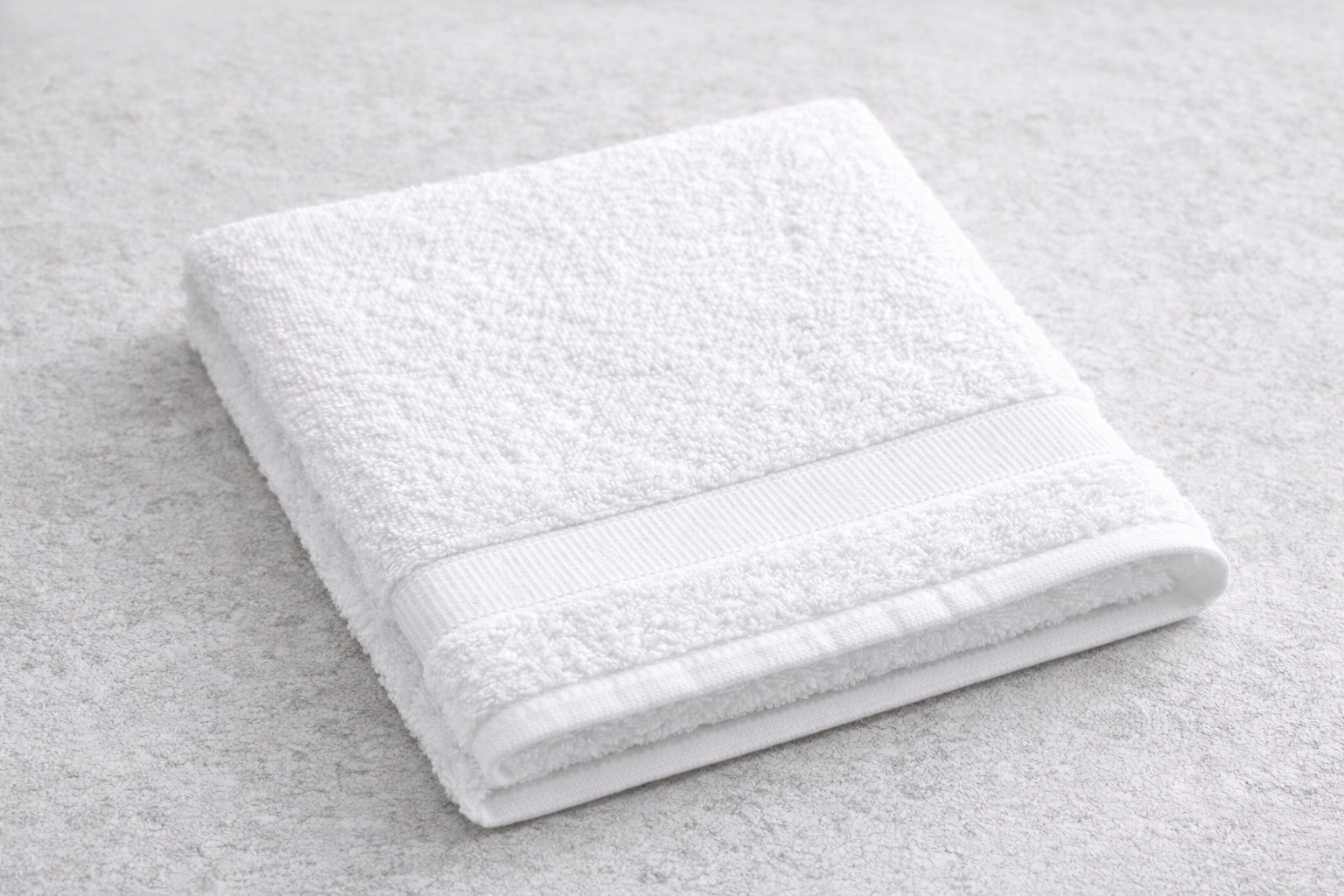 Folded white bath towel on a white textured surface.
