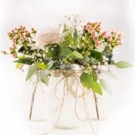 White floral arrangement with green leaves in a glass jar on a metal stand with a ribbon bow