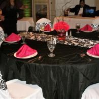 Round banquet table with black tablecloth, pink napkins, floral centerpieces, and white chairs in a dining room