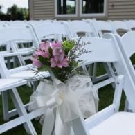 White chairs decorated with pink flowers and white ribbons at an outdoor wedding ceremony