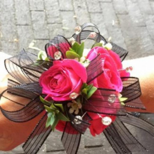 Pink rose corsage with black ribbon and greenery on a cobblestone surface