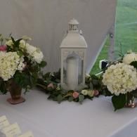 White lantern centerpiece with white flowers and greenery on a decorated table