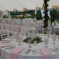 Outdoor banquet tables set with pink ribbons and glassware under a white tent