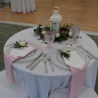 Round banquet table set with white and pink place settings, floral centerpieces, and a lantern centerpiece