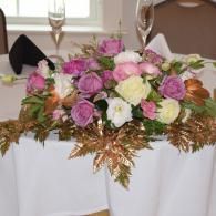 Floral centerpiece with pink, purple, and white roses on a white tablecloth at a formal setting