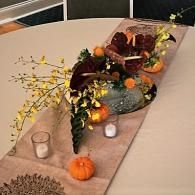 Autumn tablescape with gourds, dark grapes, yellow flowers, candles, and a burlap runner on a round table