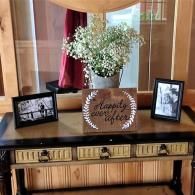 Decorated console table with flowers, framed photos, and a “happy place” sign in front of a mirror