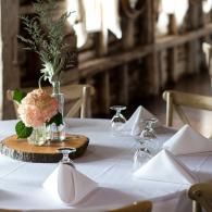 Elegant dining table set with white linens, folded napkins, stemware, and a floral centerpiece on a wooden tray