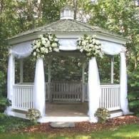 White gazebo decorated with white flowers and draped fabric in a wooded garden