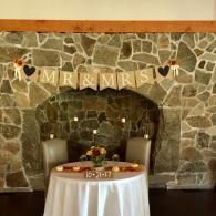 Stone fireplace backdrop with “Mr & Mrs” banner and a small round table in front