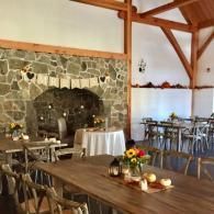 Rustic dining room with stone fireplace, wooden beams, and set tables with flowers