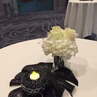 Table centerpiece with white flowers and a lit candle on a black leaf-shaped base