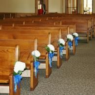 Church pews decorated with white flowers and blue ribbons in an aisle