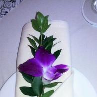 Purple flower on a white folded napkin, centered on a table setting